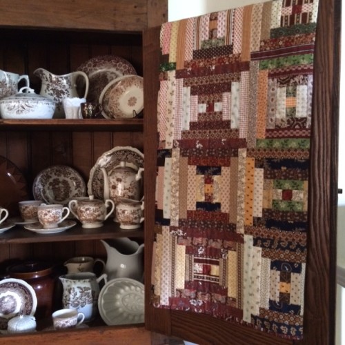 A collection of brown transferware dishes complements this Courthouse Steps quilt