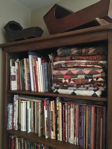 some antique quilts:tops folded on a bookshelf at the studio.