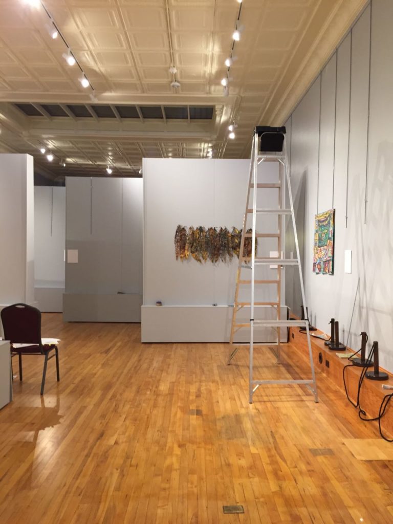 The first pieces go up. The "lines" on the right-hand wall are the hanging rods that will support the art quilts.